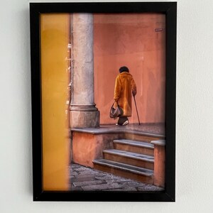 May include: A person in a brown coat walks down a set of stairs in a building with yellow and orange walls.