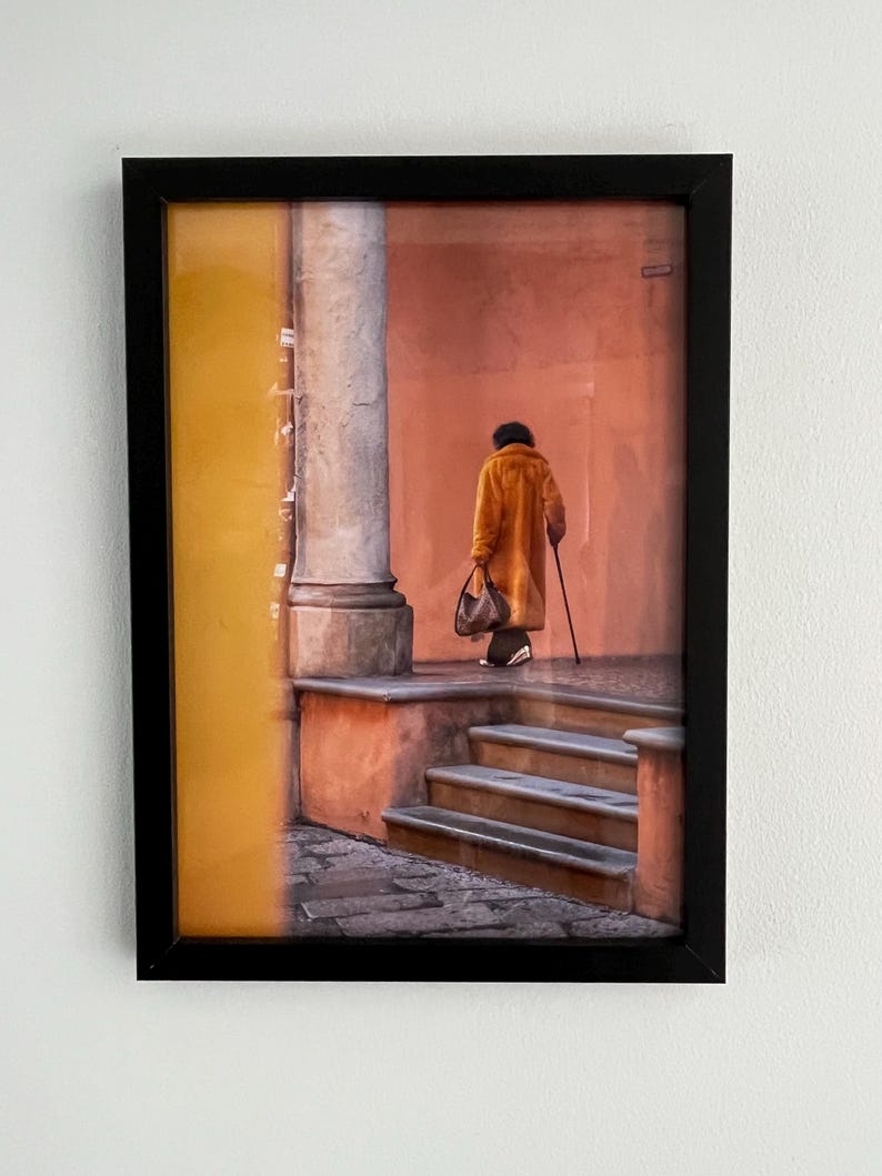 May include: A person in a brown coat walks down a set of stairs in a building with yellow and orange walls.