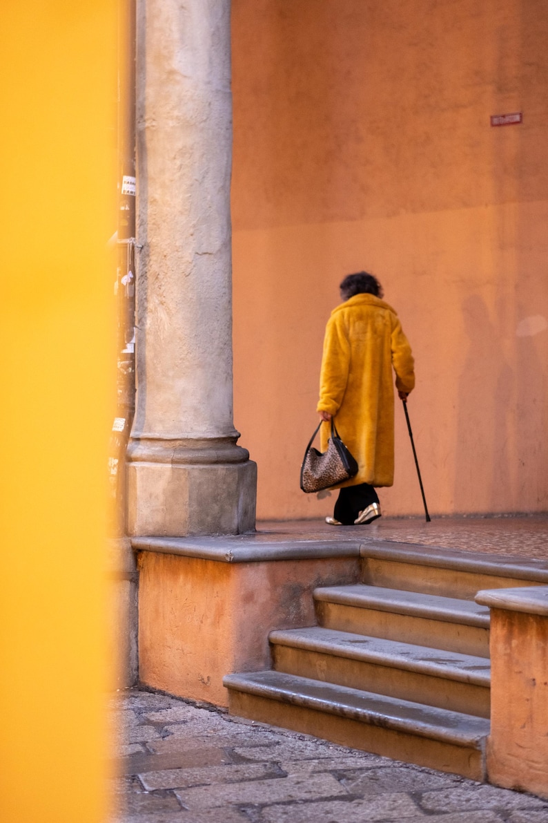 May include: A person wearing a yellow coat walks down a set of stairs with a handbag and a cane.