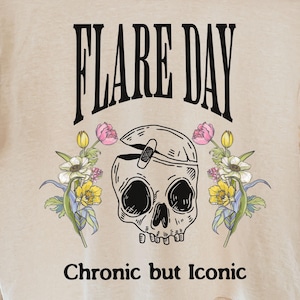 Puede incluir: Camiseta color crema con la frase "FLARE DAY" en negro, sobre un gráfico de calavera con una venda y detalles florales. La frase "Chronic but Iconic" está impresa debajo.