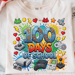 Könnte beinhalten: Cremefarbenes T-Shirt mit einer farbenfrohen Grafik, die 100 Schultage feiert. Das Design enthält den Text "100 DAYS OF SCHOOL" mit Retro-Videospiel-Controllern, pixeligen Herzen und Blitzen. Das Shirt ist aus einem weichen Material.