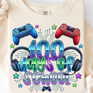 Op de afbeelding: Crèmekleurige sweatshirt met een kleurrijke afbeelding ter viering van 100 schooldagen. Het ontwerp bevat blauwe en rode gamecontrollers, koptelefoons, sterren en de tekst "100 Days of School".