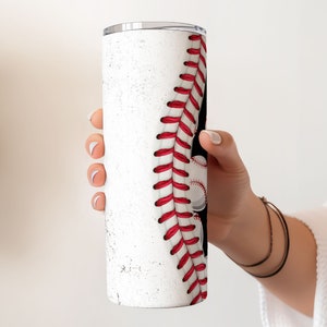May include: White stainless steel tumbler with a baseball design. The tumbler has a red and white baseball stitch design on the side.