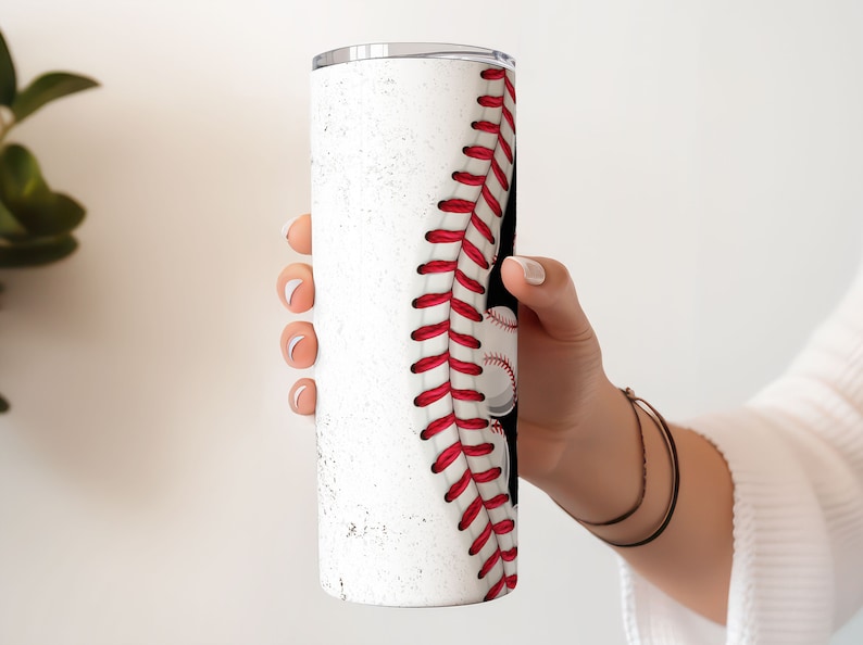 May include: White stainless steel tumbler with a baseball design. The tumbler has a red and white baseball stitch design on the side.