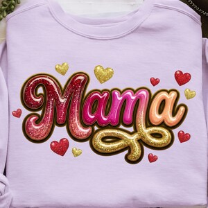 May include: A light purple sweatshirt with the word "Mama" in a glittery, 3D design. The word is outlined in brown and surrounded by red and gold glitter hearts. The sweatshirt is a casual, comfortable style.
