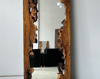 May include: A large, rectangular mirror with a natural wood frame. The frame has a unique, organic shape with a live edge design. The mirror is reflecting a room with furniture and a light fixture.