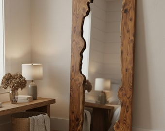 May include: A full-length, rectangular mirror with a natural wood frame. The frame has a live edge design, with the wood's natural shape forming the border. The mirror is placed against a neutral-colored wall, reflecting the room's interior.