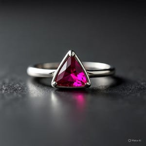 May include: A silver ring with a striking triangular, magenta gemstone. The gem is set in a sleek, contemporary design, with a polished silver band. The ring is shown against a dark backdrop, accentuating its radiant appearance.
