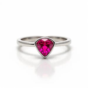 Peut inclure: Une bague en argent orn&eacute;e d'une pierre pr&eacute;cieuse rose vif en forme de bouclier. La pierre est sertie dans un sertissage &agrave; lunette, et le corps de la bague est lisse et poli. La bague est pr&eacute;sent&eacute;e sur fond blanc.