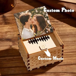 May include: A wooden music box with a custom photo and custom music. The box features a photo of a couple kissing. The box has decorative floral patterns and a musical note symbol.