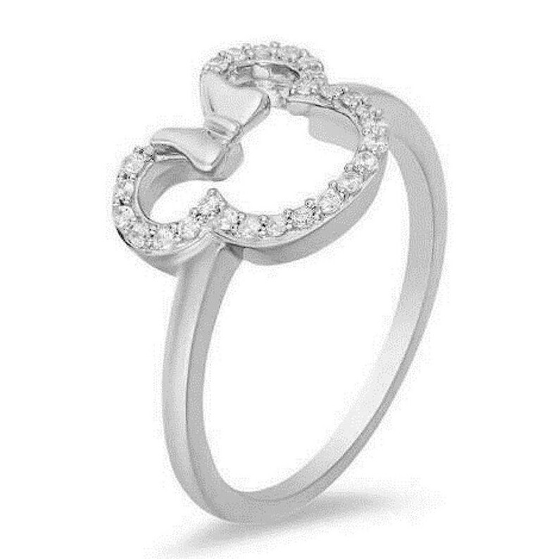 Puede incluir: Un anillo de plata con un lazo de cristal transparente y un contorno de cabeza de Mickey Mouse. El anillo est&aacute; engastado con peque&ntilde;os cristales transparentes.