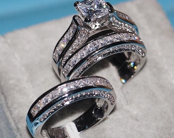 Puede incluir: Un anillo de compromiso de plata con una piedra central grande de corte cuadrado y piedras más pequeñas engastadas en pavé alrededor de la banda.