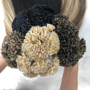 Op de afbeelding: Een close-up van een bundel haar extensions in verschillende tinten bruin en blond. De extensions zijn in een cirkelvormige opstelling geplaatst en hebben een textuur en een golvend uiterlijk.