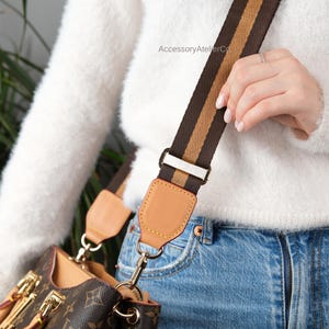 May include: Brown and tan striped bag strap with gold-tone hardware attached to a brown and tan monogram handbag. The bag strap is attached to a brown and tan monogram handbag. The text "The bag is not for sale" is visible.