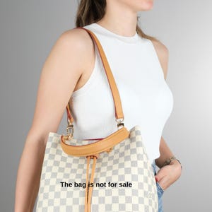 May include: A white and brown checkered tote bag with a brown leather strap and a gold chain detail. The bag has a drawstring closure and the text "The bag is not for sale" is printed on the front.