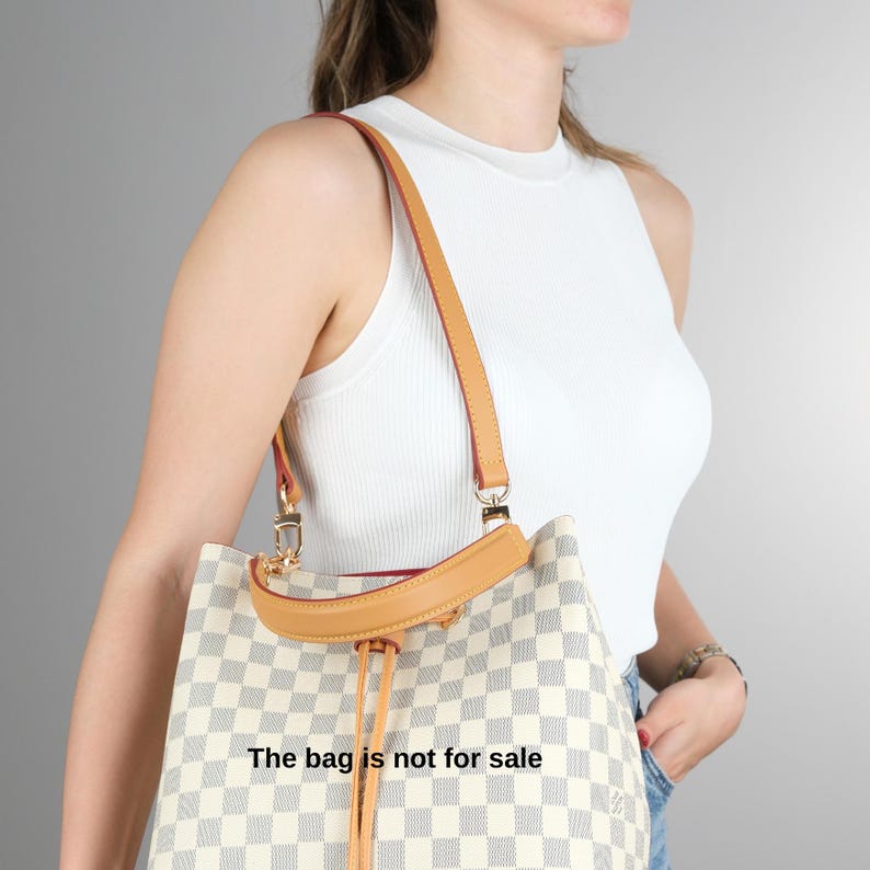 May include: A white and brown checkered tote bag with a brown leather strap and a gold chain detail. The bag has a drawstring closure and the text "The bag is not for sale" is printed on the front.