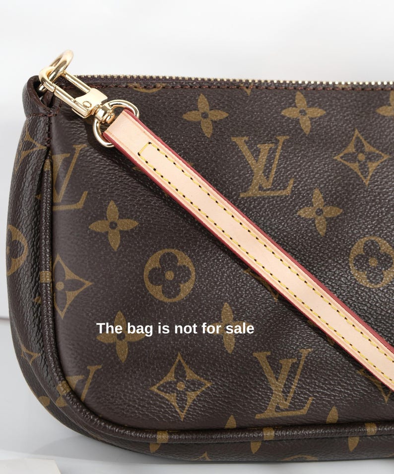 May include: Brown handbag with a repeating monogram pattern and a detachable strap. The bag features gold-tone hardware and a light-colored strap with red stitching. The text "The bag is not for sale" is visible on the bag.