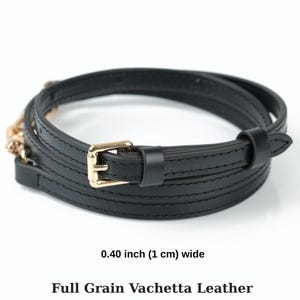 May include: A black leather belt, 1 cm wide, with a gold-coloured buckle. The belt is made of full-grain vachetta leather and is wrapped in a spiral. The text on the image reads: 0.40 inch (1 cm) wide, Full Grain Vachetta Leather.