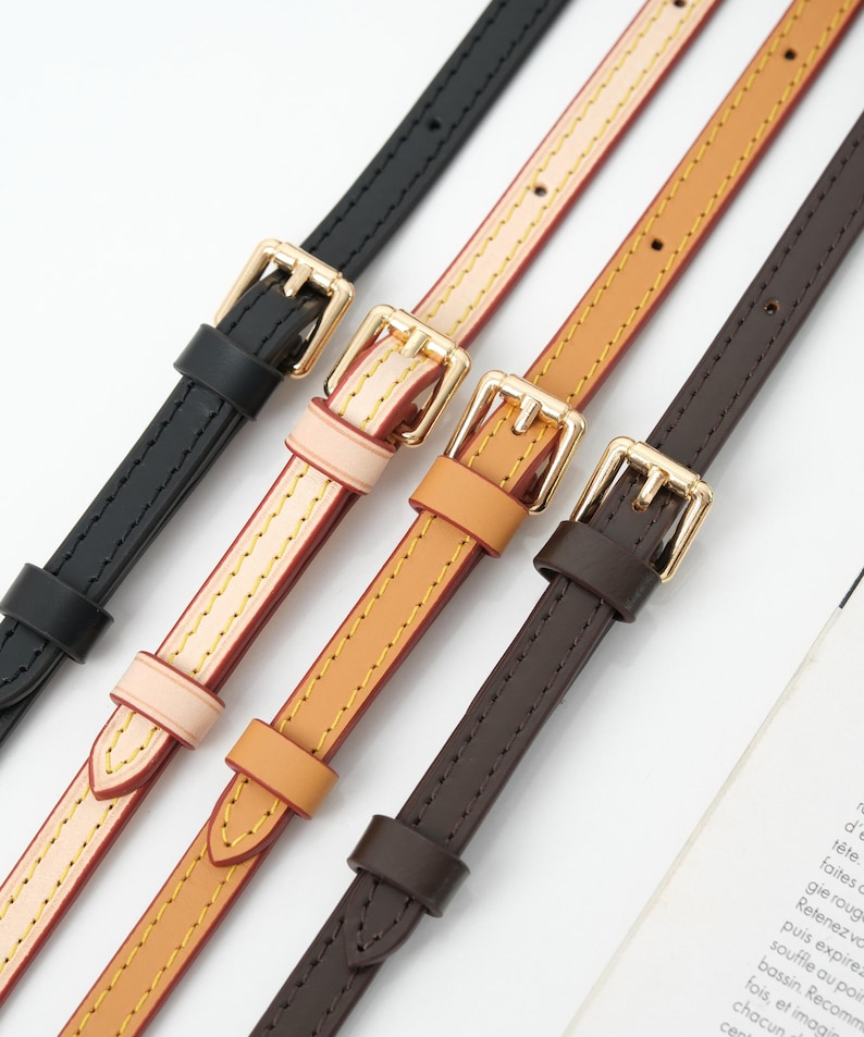 May include: Close-up of four leather bag straps in black, light pink, tan, and dark brown. Each strap has a gold-coloured metal buckle and is stitched with a contrasting thread. The straps are angled diagonally across the frame.