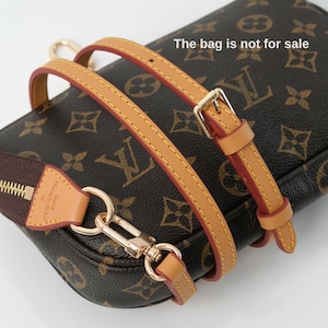 May include: A brown and tan handbag with a gold-tone clasp and strap. The bag has a repeating pattern of interlocking letters and floral designs. The strap is tan with red edges and gold stitching. The zipper is brown with a gold zipper pull.