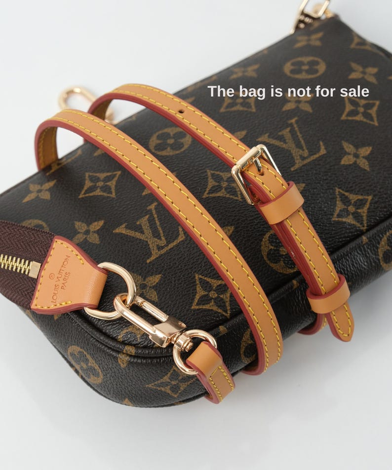 May include: A brown and tan handbag with a gold-tone clasp and strap. The bag has a repeating pattern of interlocking letters and floral designs. The strap is tan with red edges and gold stitching. The zipper is brown with a gold zipper pull.