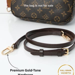 May include: A brown leather handbag strap with gold-tone hardware. The strap is made of full-grain vachetta leather and features a buckle and clasp. The bag is not for sale.