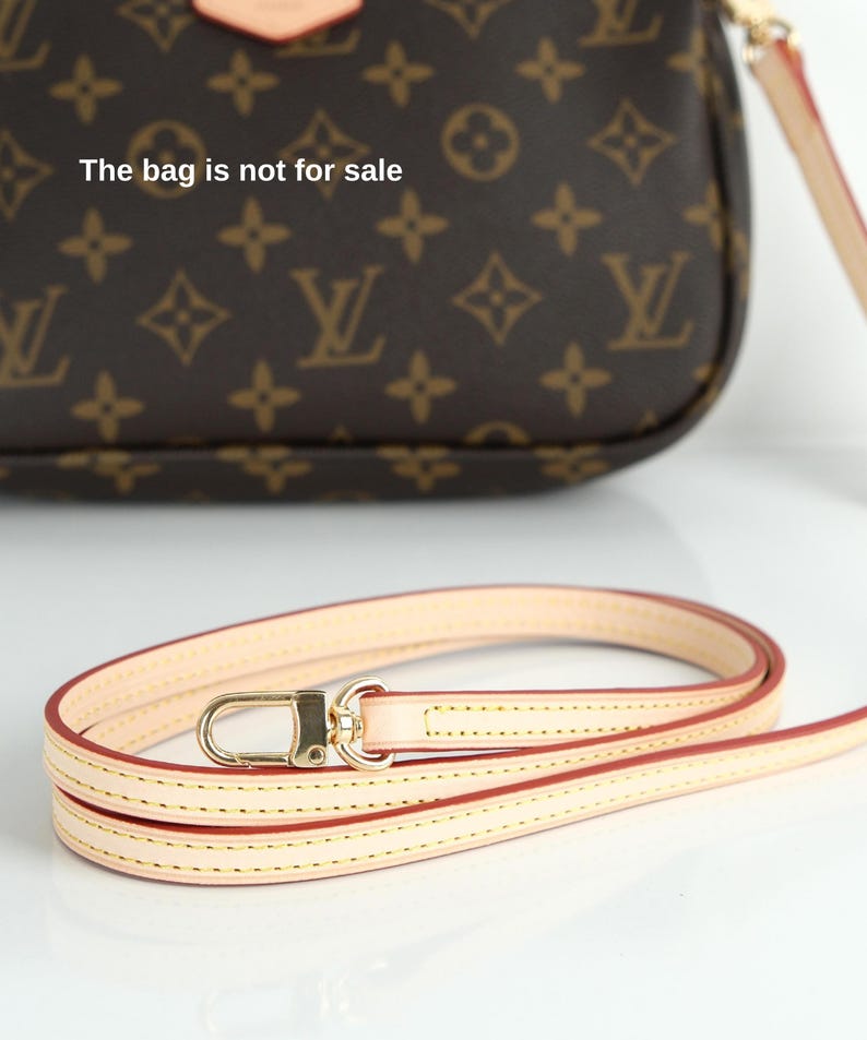 May include: A light beige leather purse strap with gold-colored hardware. The strap is thin and has a red edge. The background shows a brown purse with a repeating pattern and the text "The bag is not for sale".