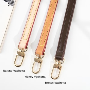 May include: Three leather bag straps in Natural Vachetta, Honey Vachetta, and Brown Vachetta. Each strap has gold-colored metal hardware and is stitched along the edges. The straps are displayed against a white background.