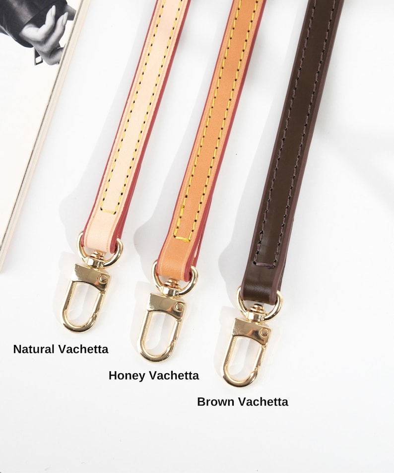 May include: Three leather bag straps in Natural Vachetta, Honey Vachetta, and Brown Vachetta. Each strap has gold-colored metal hardware and is stitched along the edges. The straps are displayed against a white background.