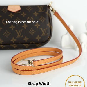 May include: A tan leather purse strap with a gold-colored clasp. The strap is 0.4 inches (1 cm) wide and made of full-grain vachetta leather. The bag in the background is not for sale.