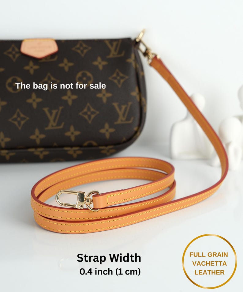 May include: A tan leather purse strap with a gold-colored clasp. The strap is 0.4 inches (1 cm) wide and made of full-grain vachetta leather. The bag in the background is not for sale.