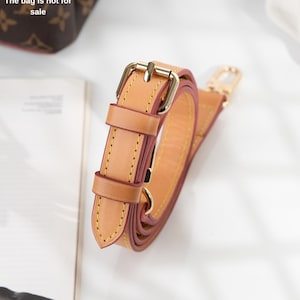 May include: A brown leather strap with a gold buckle and a gold hook. The strap is folded in half and the buckle is closed.