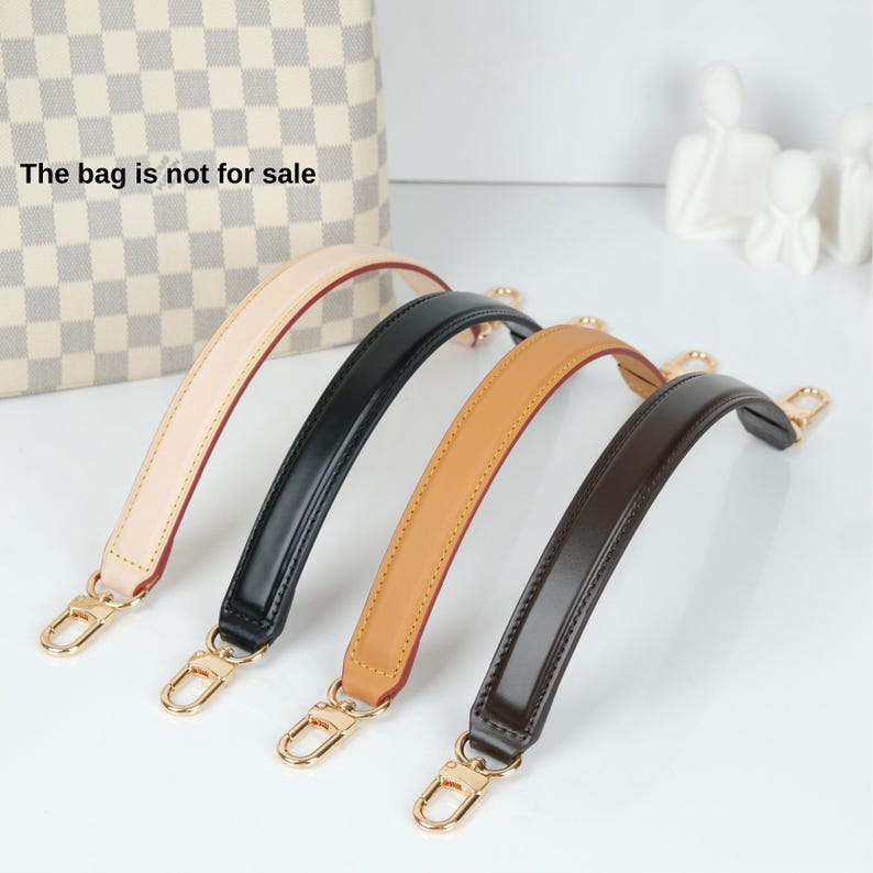 May include: Three different colored leather handbag straps with gold hardware. The straps are beige, black, and brown.