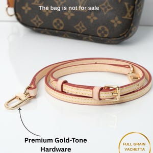 May include: A tan leather purse strap with gold-tone hardware. The strap is rolled up and has a gold-tone clasp and buckle. The text "Premium Gold-Tone Hardware" is visible. The bag is not for sale.