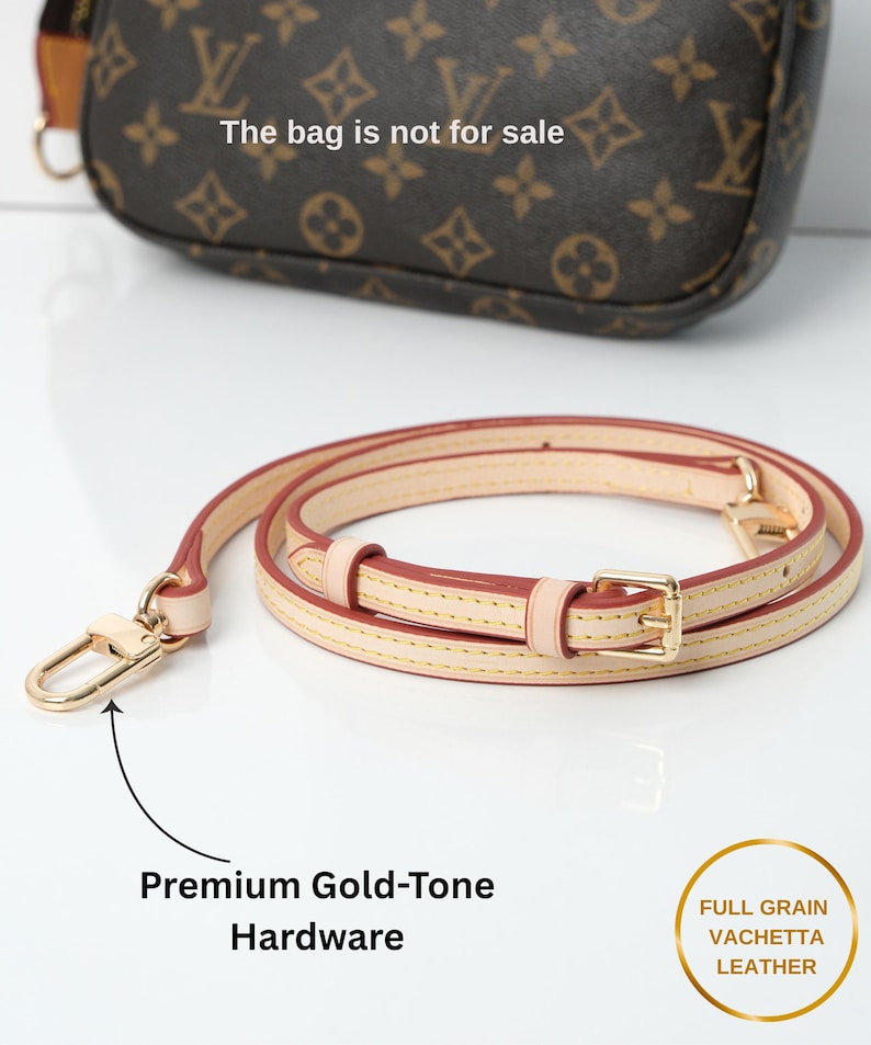 May include: A tan leather purse strap with gold-tone hardware. The strap is rolled up and has a gold-tone clasp and buckle. The text "Premium Gold-Tone Hardware" is visible. The bag is not for sale.