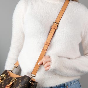以下が含まれることがあります： ゴールドカラーのバックルと金具が付いた、ライトブラウンのレザーショルダー ストラップが、ブラウンとタンのハンドバッグに取り付けられています。 バッグにはモノグラム柄があります。「The bag is not for sale」というテキストが表示されています。