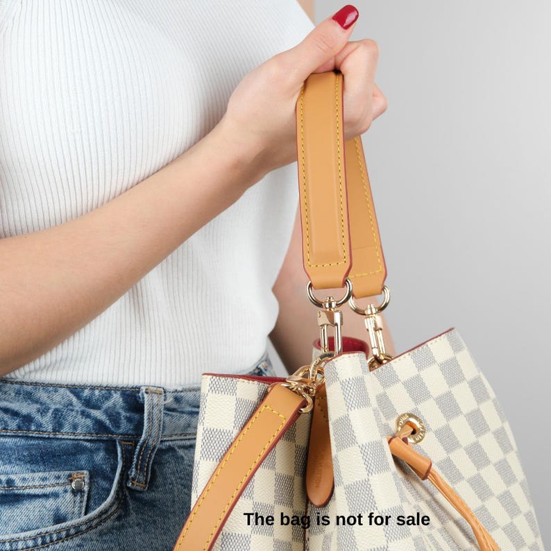 May include: A white and black checkered handbag with a brown leather strap and gold hardware. The bag has a drawstring closure and a top handle. The bag is not for sale.