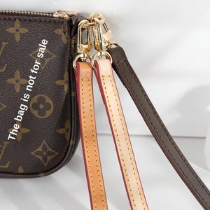 Pode incluir: Bolsa marrom com monograma com ferragens douradas e três alças removíveis em bege, rosa e marrom escuro. O texto "The bag is not for sale" é visível na bolsa.