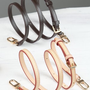 May include: Two leather purse straps. One is dark brown with gold-coloured hardware. The other is light beige with red edges and gold-coloured hardware. Both straps have a buckle and a clasp.