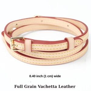 May include: A coiled leather strap in a light hue, with a gold-coloured buckle. The strap is 1 cm wide and has red edges and gold stitching. The text at the bottom reads "Full Grain Vachetta Leather".