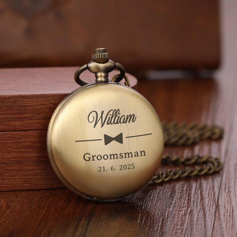 May include: A bronze-finished pocket watch. The watch face is engraved with the name "William", a bow tie symbol, the word "Groomsman", and the date "21. 6. 2025". The watch has an attached chain.