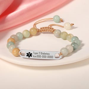 Könnte beinhalten: Armband mit Perlen und einem silbernen ID-Anhänger. Das Armband hat pastellfarbene Perlen. Der ID-Anhänger ist mit den Worten "Type 2 Diabetes" und "Ice:000-000-0000" sowie einem medizinischen Symbol graviert.