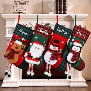Könnte beinhalten: Vier personalisierte Weihnachtsstrümpfe mit verschiedenen Figuren. Die Strümpfe sind rot und grün mit einem karierten Muster. Die Figuren sind ein Rentier, der Weihnachtsmann, ein Schneemann und ein Pinguin. Die Strümpfe hängen an einem Kaminsims.