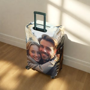 May include: A white suitcase cover with a photo of a couple printed on it. The couple is smiling and hugging. The suitcase cover has a black handle.