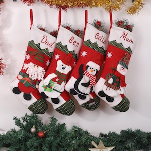 May include: Four Christmas stockings with red and white designs, each featuring a different character: Santa, a polar bear, a penguin, and a snowman. The stockings are labeled "Dad", "Ben", "Bella", and "Mum".