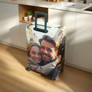 May include: A luggage cover with a photo of a couple smiling and hugging. The cover is black and has a zipper closure.