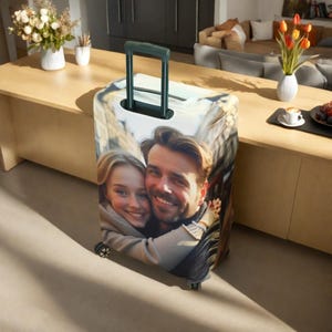 May include: A luggage cover with a photo of a couple smiling and hugging. The cover is white with a colorful cityscape in the background.