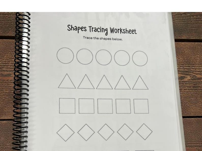 May include: A spiral-bound worksheet with the title "Shapes Tracing Worksheet." The worksheet features rows of circles, triangles, squares, and diamonds for tracing. The background is a wooden surface.