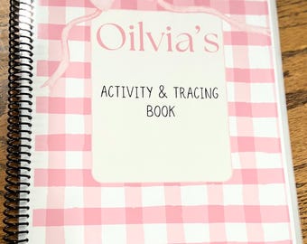 May include: A spiral-bound activity and tracing book with a pink gingham pattern cover. The cover features a white rectangle with the name "Olivia's" and the text "Activity & Tracing Book" in black font, and a pink bow.