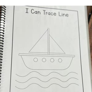 May include: A spiral-bound workbook page with the text "I Can Trace Line." The page features a dotted line drawing of a sailboat with a triangular sail and wavy lines representing water. The image is in black and white.